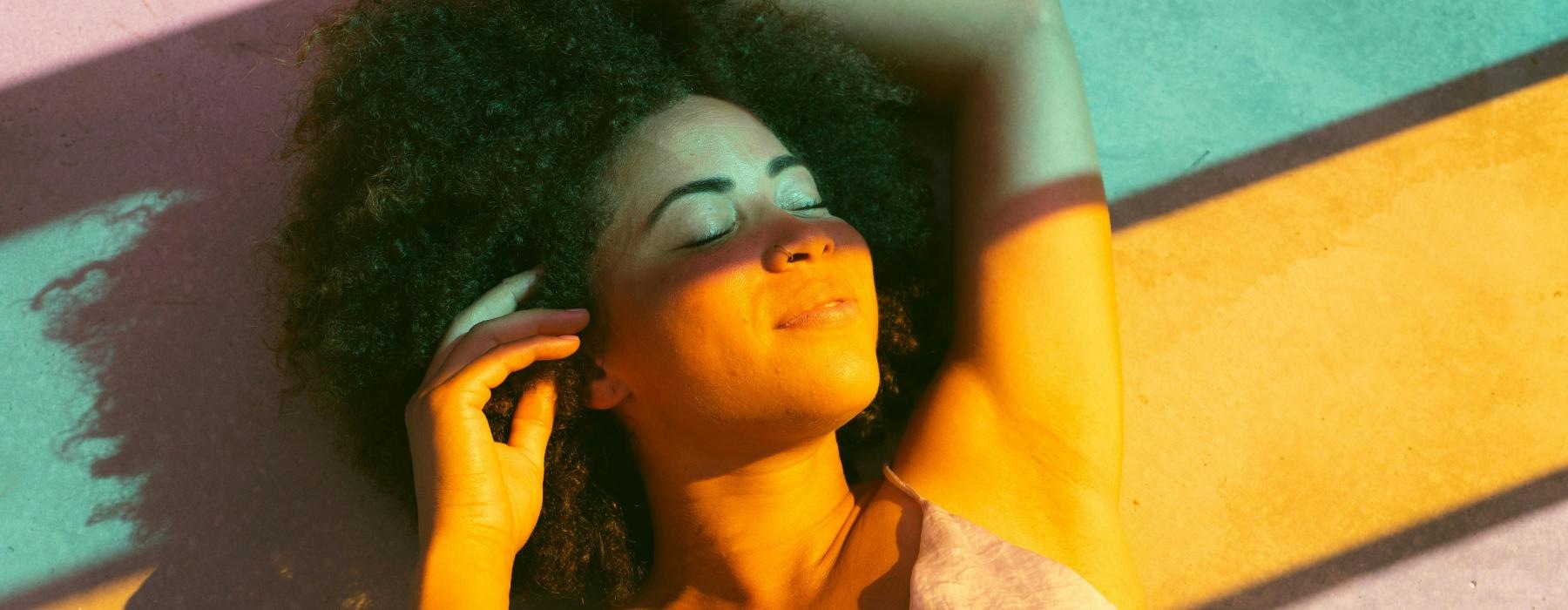 woman lying on a floor with sunlight pouring through colorful glass